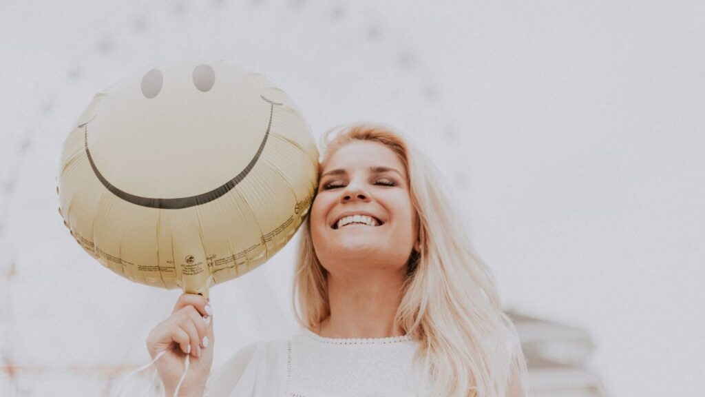 Lady smiling holding a yellow balloon with a smiley face